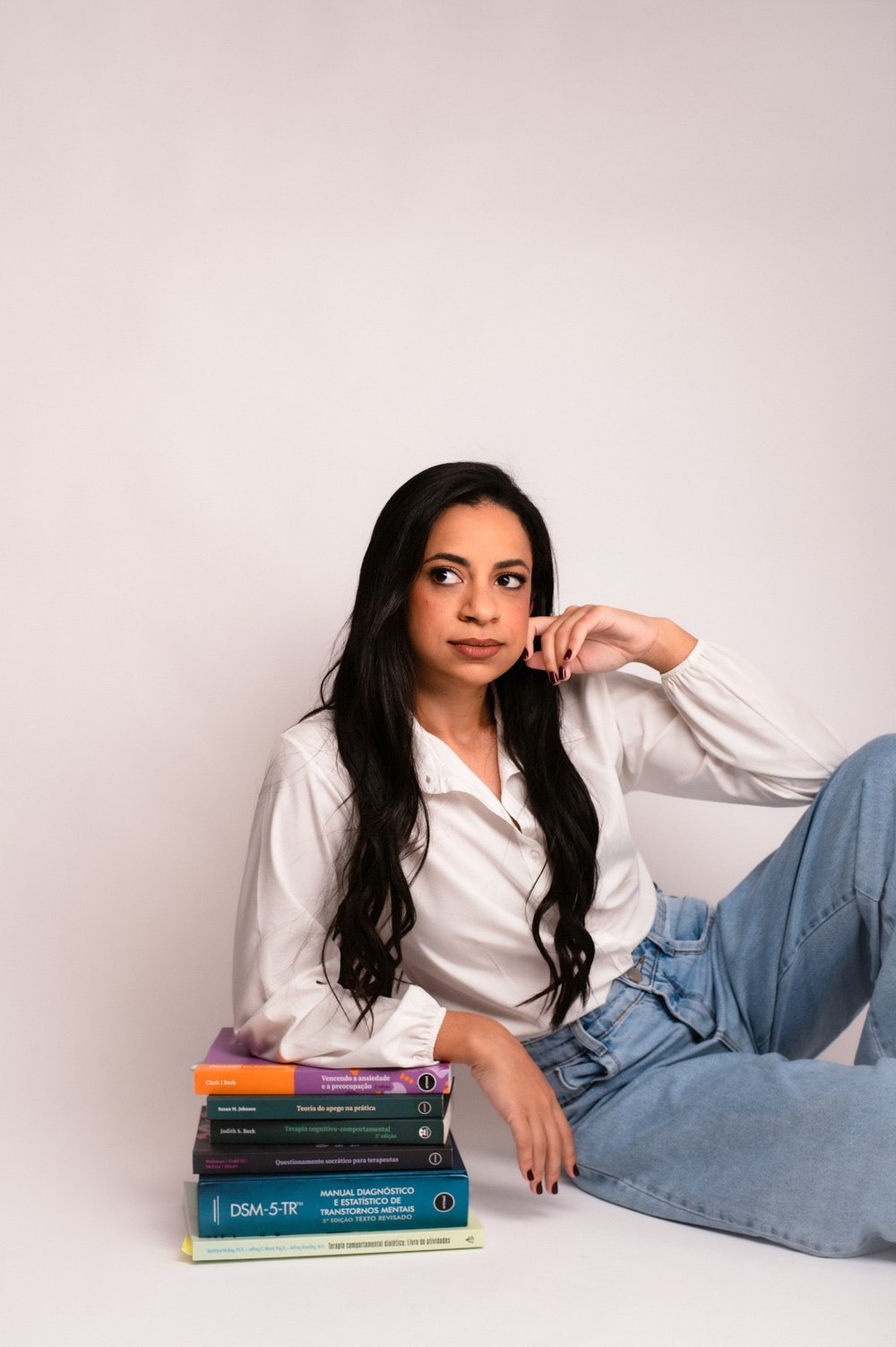 Larissa Rezende sentada ao lado de sua estante de livros de psicologia